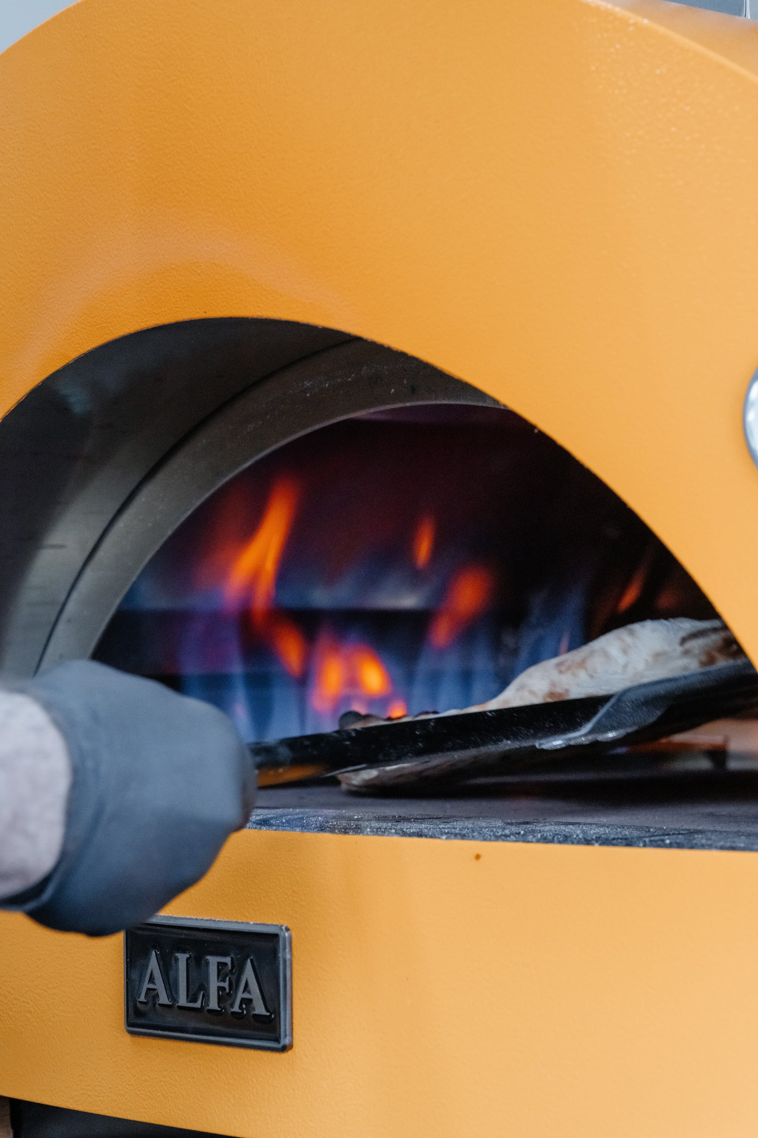 The Forno Via pizza oven glowing with fire as fresh pizzas are prepared