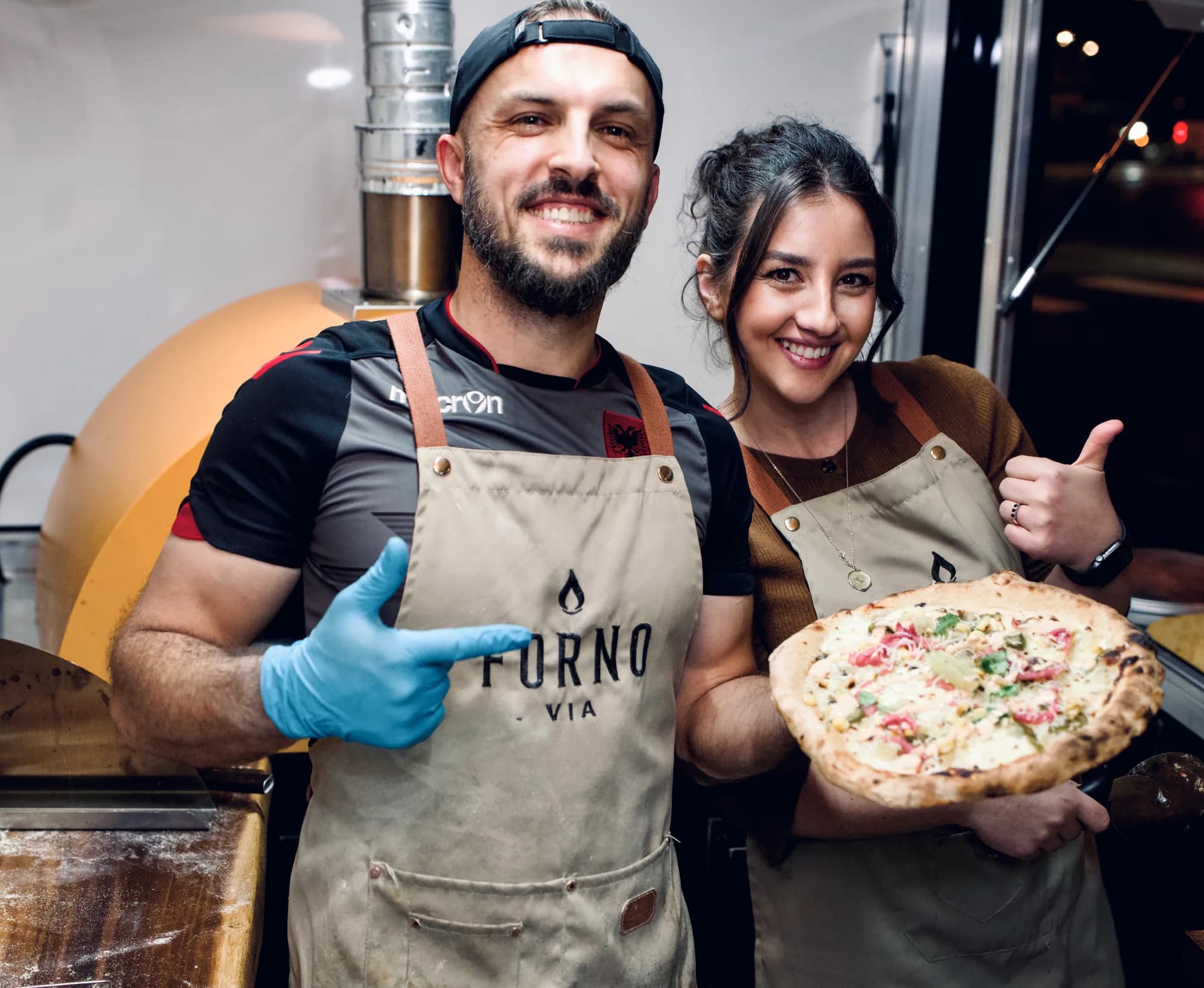 Forno Via catering team holding a freshly prepared pizza beside the mobile oven
